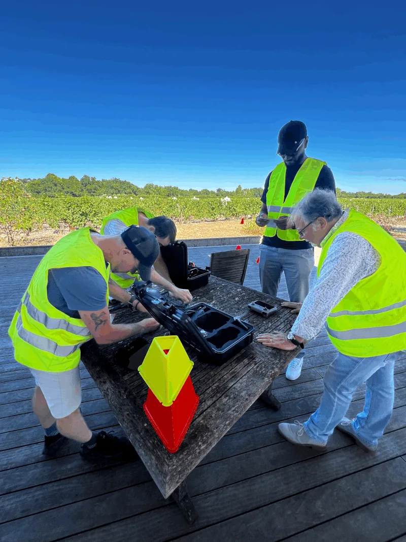 Trainees in high-visibility vests assembling a drone on a table during the outdoor practical session — Dronexperts drone pilot training