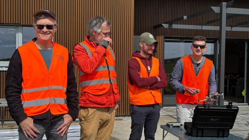 Group of trainees in high-visibility vests in the field, drone and remote controller in hand, transport case open on the table — Dronexperts drone pilot training