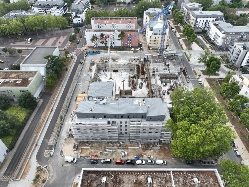 Drone construction site monitoring — aerial view of the foundations and structural shell of a housing development with two tower cranes at work, Dronexperts