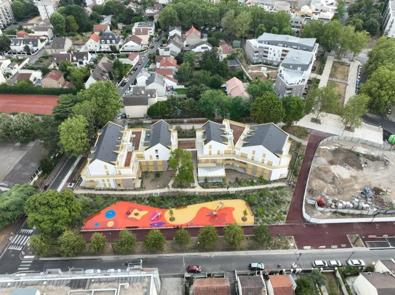 Drone construction site monitoring — aerial view of a completed residence with landscaped courtyard and colourful playground in an urban setting, Dronexperts
